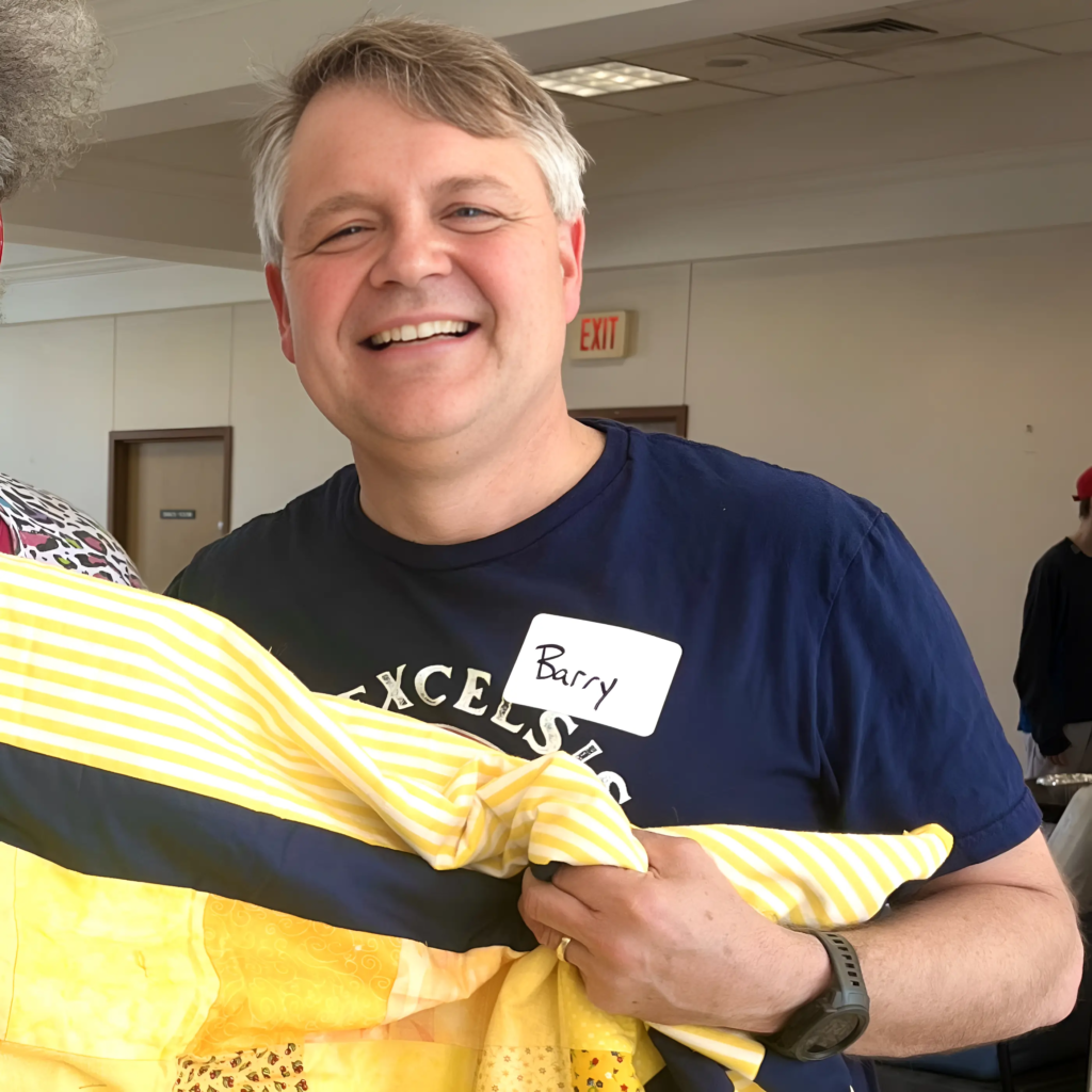 Barry smiling while giving a blanket to a guest that had recently moved into her apartment as a welcoming home basket.