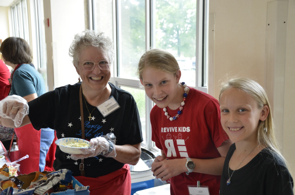 Regular generous lunch sponsor Sueann and two young volunteers serving ready to serve lunch.